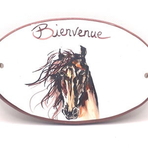 May include: Oval ceramic sign with a brown horse head illustration and the text "Bienvenue" in cursive. The sign has a brown border and two holes for hanging.