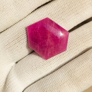 May include: A hexagonal pink gemstone with a smooth, polished surface. The gemstone has a slight shimmer and is set against a white background.