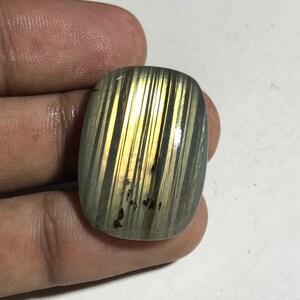 May include: A green and gold gemstone with a striated pattern. The gemstone is cut into a rectangular shape and has a smooth, polished surface.