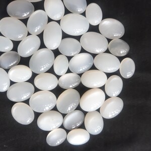 May include: A collection of white oval moonstone cabochons. The stones are smooth and polished, with a subtle iridescent sheen.