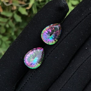 May include: Two pear-shaped iridescent gemstones with a rainbow of colors, including pink, green, and blue.