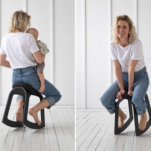 Puede incluir: Una mujer se sienta en una silla mecedora negra con un asiento curvo y una base ancha. Lleva pantalones vaqueros azules y una camiseta blanca. En la otra imagen, la mujer est&aacute; sentada en la misma silla, pero no est&aacute; sosteniendo un beb&eacute;.