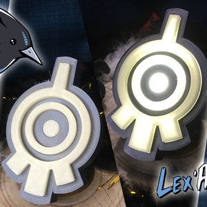 Pode incluir: Dois símbolos impressos em 3D, brancos e cinzentos, com um design circular e um círculo central. O símbolo à direita está iluminado com uma luz branca. O texto "Lex'Art" é visível no canto inferior direito da imagem.