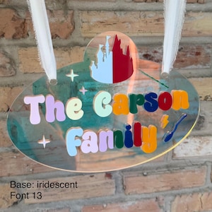 May include: Iridescent family name sign with the text "The Carson Family" in colorful bubble letters. The sign features a castle graphic and star accents, with a lightning bolt and a spoon. White ribbon is attached for hanging.