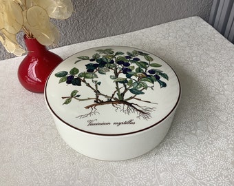 May include: White ceramic round dish with a botanical illustration of blueberries and leaves. The dish has a brown rim and the text "Vaccinium myrtillus" is printed on the bottom.