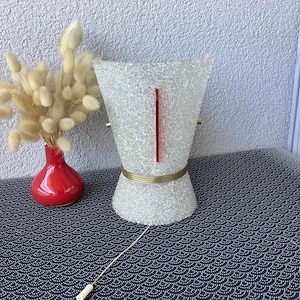 Peut inclure: Une lampe de table vintage avec un abat-jour en verre texturé et moucheté et un accent rouge. La lampe a une bande de couleur laiton au milieu et un cordon blanc avec un interrupteur. Un petit vase rouge avec des fleurs séchées est à gauche.