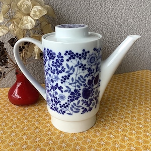 Può includere: Caffettiera in ceramica bianca con un motivo floreale blu e bianco. La caffettiera ha un beccuccio e un manico.