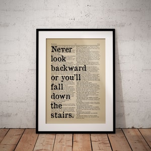 May include: A black and white typography print featuring the quote "Never look backward or you'll fall down the stairs." The quote is printed on a vintage dictionary page.