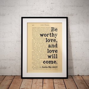 Puede incluir: Una página de libro vintage con una imagen en blanco y negro de una impresión enmarcada. La impresión presenta una cita del libro "Mujercitas" de Louisa May Alcott. La cita dice "Sé digno de amor, y el amor vendrá."