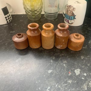 Peut inclure: Un ensemble de cinq pots en grès vintage dans des tons variés de brun et de beige. Le lot comprend trois pots cylindriques plus hauts à col étroit et deux pots plus courts et larges avec des ouvertures réduites, tous avec une finition émaillée.