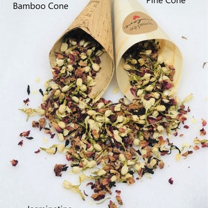 May include: Two bamboo cones filled with dried jasmine and rose petals. The cones are labeled "Bamboo Cone" and "Pine Cone". The text "Spread the Love" is printed on the pine cone. The petals are scattered on a white surface with the text "Jasminetine" printed below.