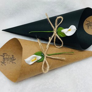 May include: Two wedding favor cones, one brown and one black, with white calla lilies and twine bows. The brown cone has a sticker that says "Happily Ever After".