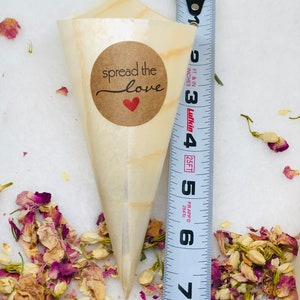 May include: A small, brown paper cone with a brown circle sticker that says "spread the love" with a red heart. The cone is filled with dried flower petals and is next to a measuring tape.