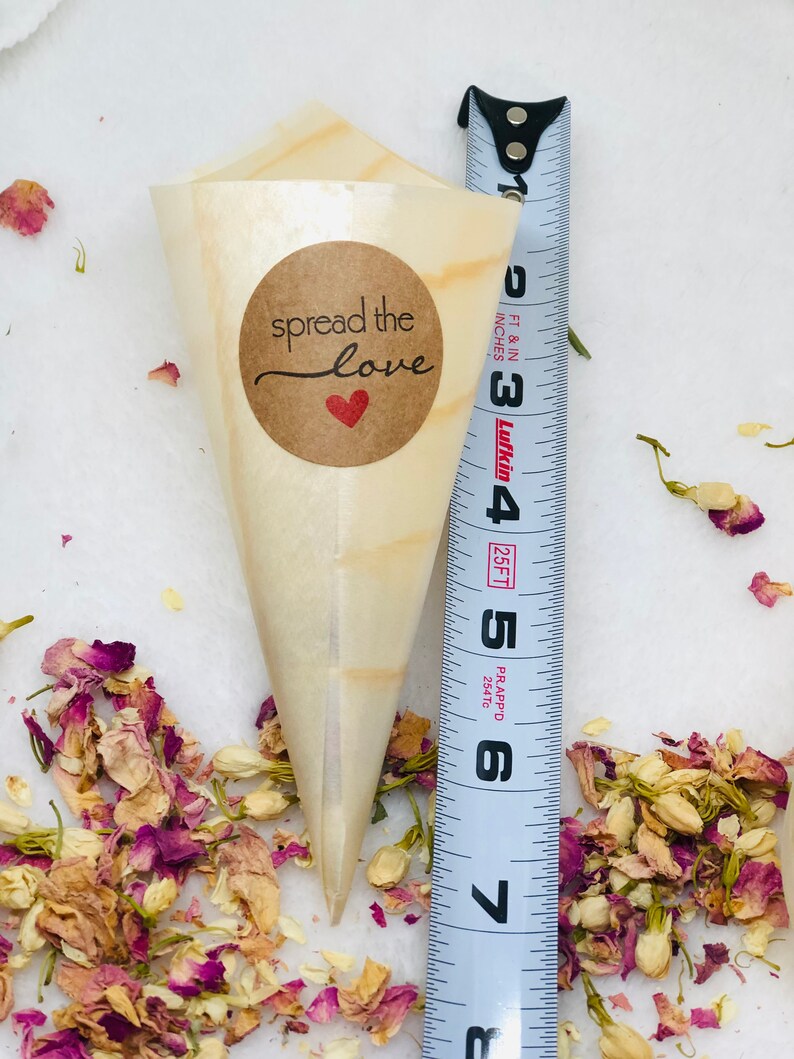 May include: A small, brown paper cone with a brown circle sticker that says "spread the love" with a red heart. The cone is filled with dried flower petals and is next to a measuring tape.