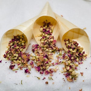 May include: Three wooden cones filled with dried rose petals and white flowers. The cones are arranged in a triangle shape on a white surface.