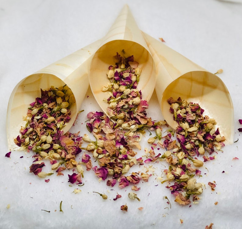 May include: Three wooden cones filled with dried rose petals and white flowers. The cones are arranged in a triangle shape on a white surface.