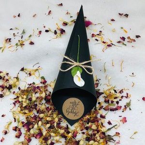 May include: Black paper cone filled with dried flower petals for a wedding ceremony. The cone has a brown paper circle attached with the text "Just Married" written in white.