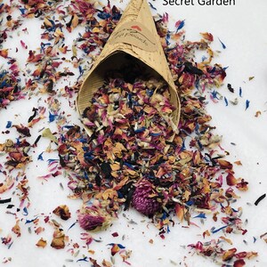 May include: A paper cone filled with dried flower petals in shades of pink, purple, blue, and brown. The cone is labeled "Secret Garden".