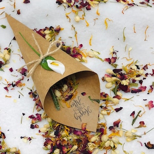 May include: A brown paper cone filled with dried flower petals, including rose petals, jasmine, and calendula. The cone has a white calla lily attached to it and a sticker that says "Happily Ever After".