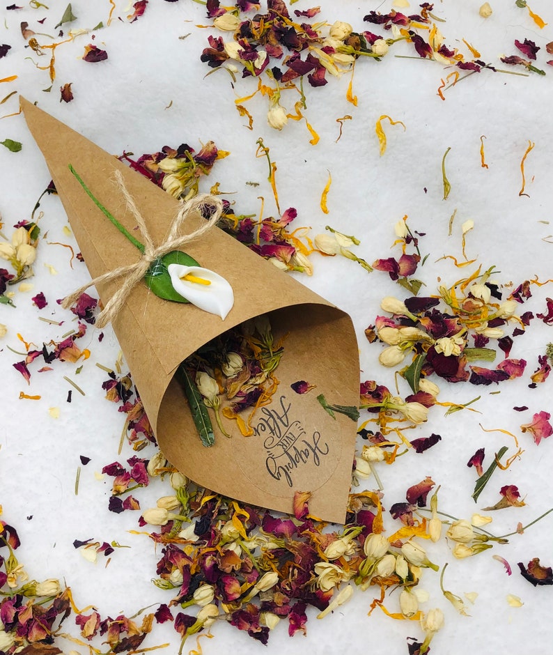 May include: A brown paper cone filled with dried flower petals, including rose petals, jasmine, and calendula. The cone has a white calla lily attached to it and a sticker that says "Happily Ever After".