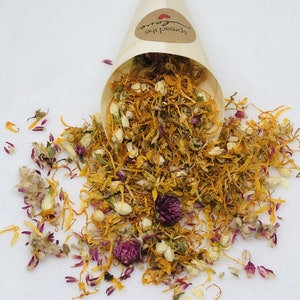 May include: A cone filled with dried flower petals, including yellow, orange, white, and purple petals. The cone is labeled "Spread the Love". The petals are scattered on a white surface with the text "Sweet Sunshine".