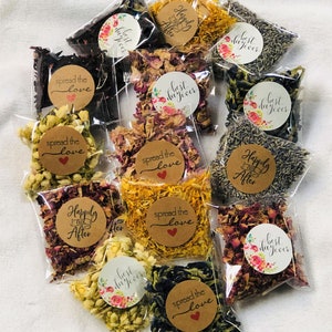 May include: Assortment of small clear bags filled with dried flower petals and herbs. Each bag has a round paper sticker with a different phrase, such as "Happily Ever After", "Spread the Love", and "Best Day Ever".