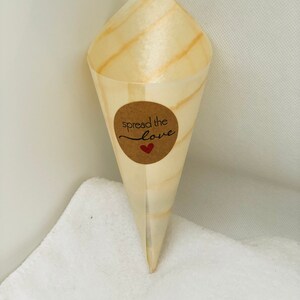 May include: A brown paper cone with a round brown sticker that says "spread the love" with a red heart. The cone is sitting on a white towel.