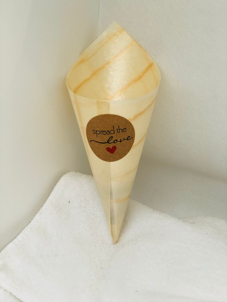 May include: A brown paper cone with a round brown sticker that says "spread the love" with a red heart. The cone is sitting on a white towel.