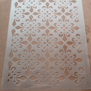 May include: White plastic stencil featuring a repeating pattern of ornate floral designs. The stencil measures approximately 11 inches in height.