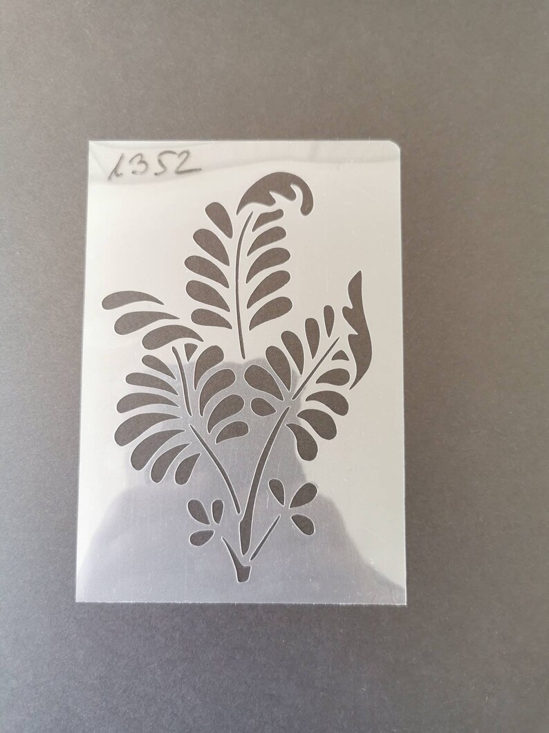 May include: A white plastic stencil with a black floral design. The stencil has the number "1352" written in the top left corner.