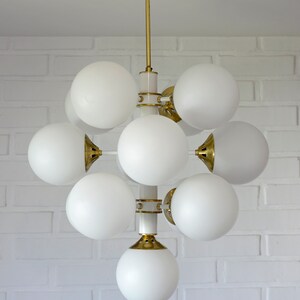 May include: A white and gold modern chandelier with multiple white globe-shaped light fixtures.