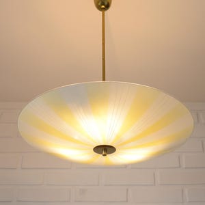 May include: A vintage, round ceiling light fixture with a yellow and white striped shade. The light has a brass-colored stem and a circular base. The shade is illuminated, casting a warm glow.