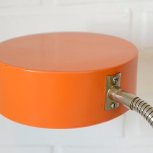 Puede incluir: L&aacute;mpara de escritorio naranja con un brazo de metal flexible y una pantalla redonda naranja.