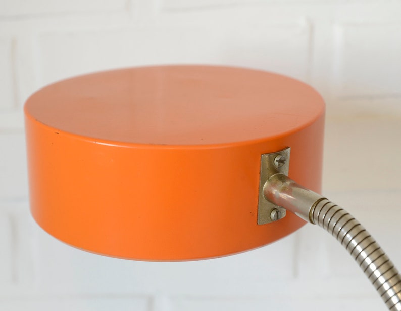 Puede incluir: L&aacute;mpara de escritorio naranja con un brazo de metal flexible y una pantalla redonda naranja.