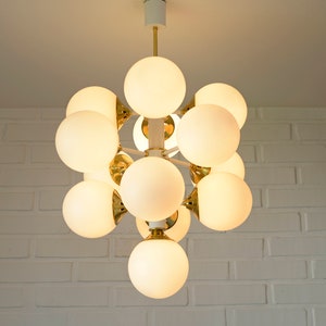 May include: A white ceiling light fixture with multiple round, white frosted glass bulbs. The fixture is made of gold metal and has a modern design.