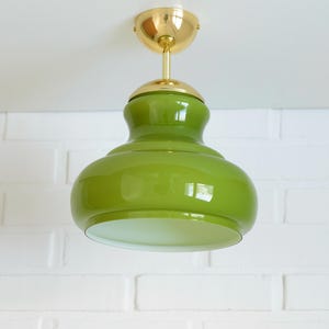 May include: A green glass pendant light with a brass ceiling fitting. The light has a rounded, bulbous shape and a white interior. The light fixture is suspended from the ceiling.
