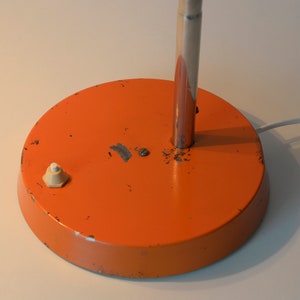 Puede incluir: Base de l&aacute;mpara de escritorio de metal naranja con un interruptor de encendido/apagado blanco. La l&aacute;mpara tiene un v&aacute;stago de metal plateado.