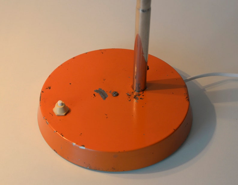 Puede incluir: Base de l&aacute;mpara de escritorio de metal naranja con un interruptor de encendido/apagado blanco. La l&aacute;mpara tiene un v&aacute;stago de metal plateado.