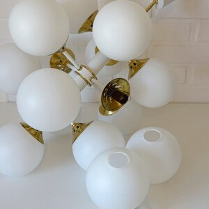 May include: A white and gold modern chandelier with multiple globe-shaped light fixtures. The chandelier is hanging from the ceiling and is made of metal.