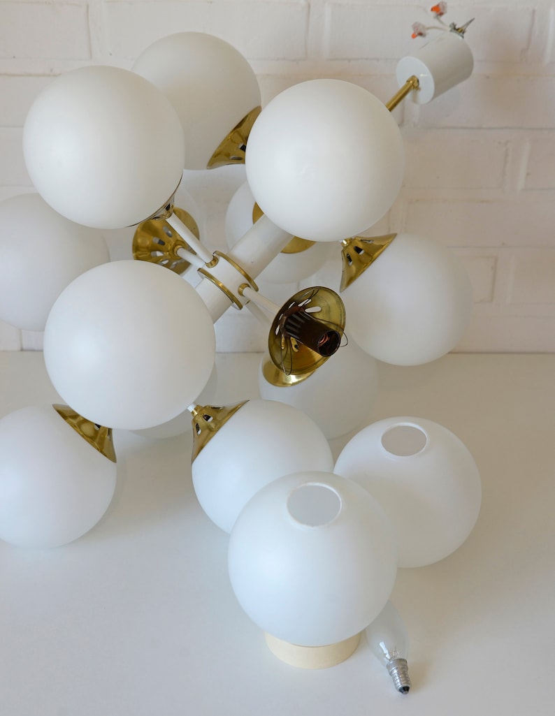 May include: A white and gold modern chandelier with multiple globe-shaped light fixtures. The chandelier is hanging from the ceiling and is made of metal.