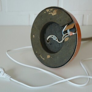 Puede incluir: La parte inferior de una l&aacute;mpara de mesa marr&oacute;n con una base de metal negro y un cable el&eacute;ctrico blanco con un enchufe. La l&aacute;mpara tiene cables expuestos.