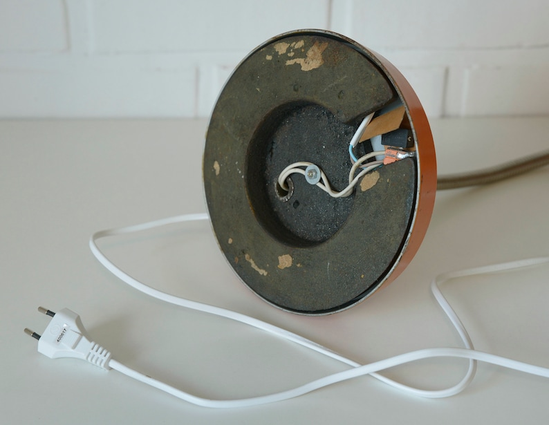 Puede incluir: La parte inferior de una l&aacute;mpara de mesa marr&oacute;n con una base de metal negro y un cable el&eacute;ctrico blanco con un enchufe. La l&aacute;mpara tiene cables expuestos.