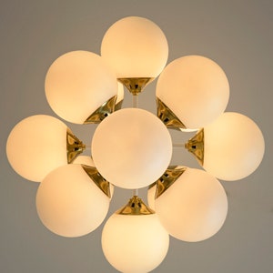 May include: A gold-toned chandelier with eight white frosted glass globes. The globes are arranged in a circular pattern and are connected by a central metal frame.