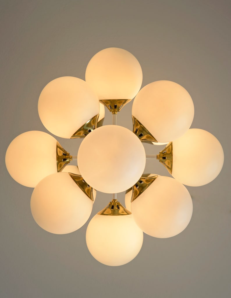 May include: A gold-toned chandelier with eight white frosted glass globes. The globes are arranged in a circular pattern and are connected by a central metal frame.