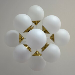 May include: A white ceiling light fixture with multiple round globes. The globes are connected to a central point with gold metal accents.