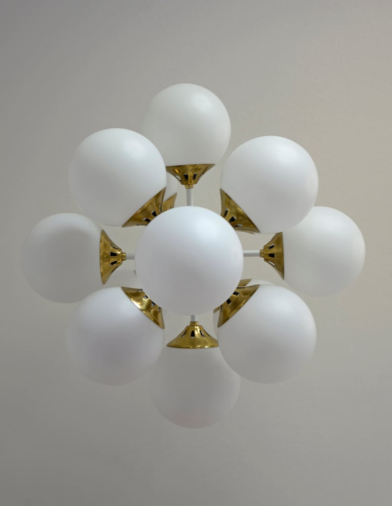 May include: A white ceiling light fixture with multiple round globes. The globes are connected to a central point with gold metal accents.