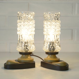 May include: Two vintage glass table lamps with textured glass shades and brown bases. The lamps are turned on and illuminated.