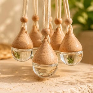 May include: A collection of hanging glass diffusers, each featuring a clear, rounded glass base filled with liquid and topped with a light-toned wooden cap shaped like a teardrop. Each diffuser is suspended by a thick, cream-colored cord.