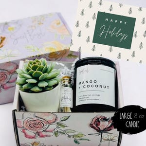 May include: A floral gift box with a succulent plant, a candle, and matches. The candle is labeled "Mango + Coconut" and is an 8 oz large candle. The gift box has a card that says "Happy Holidays".