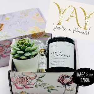 May include: A floral gift box with a succulent plant, a small bottle of matches, and a black candle with a white label that says "Mango + Coconut" and "Large 8 oz Candle". A card with gold lettering says "Yay You're a Winner!"